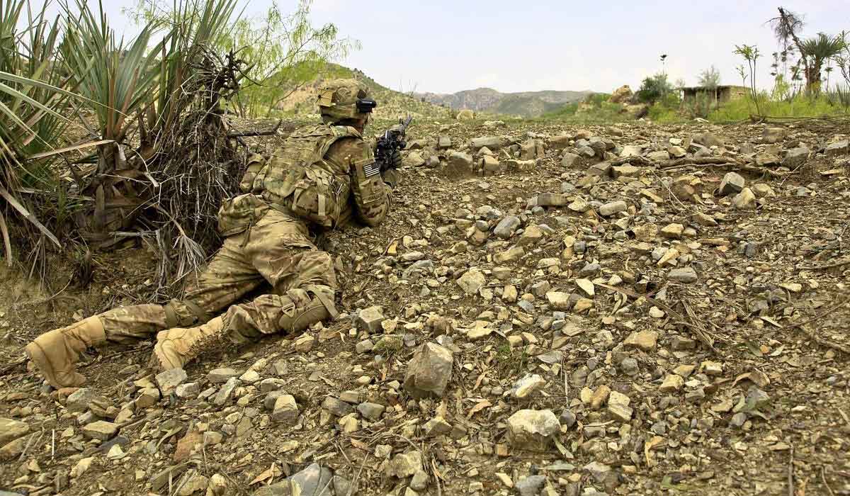 soldier crawling on mossy rocks is camouflaged in his olive green uniform.